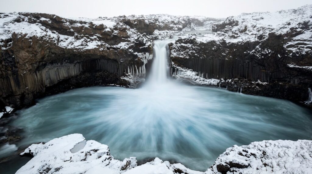 a large waterfall is surrounded by snow covered rocks