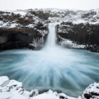 a large waterfall is surrounded by snow covered rocks