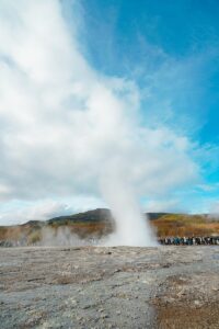 Geyser erupting with steam against a cloudy blue sky