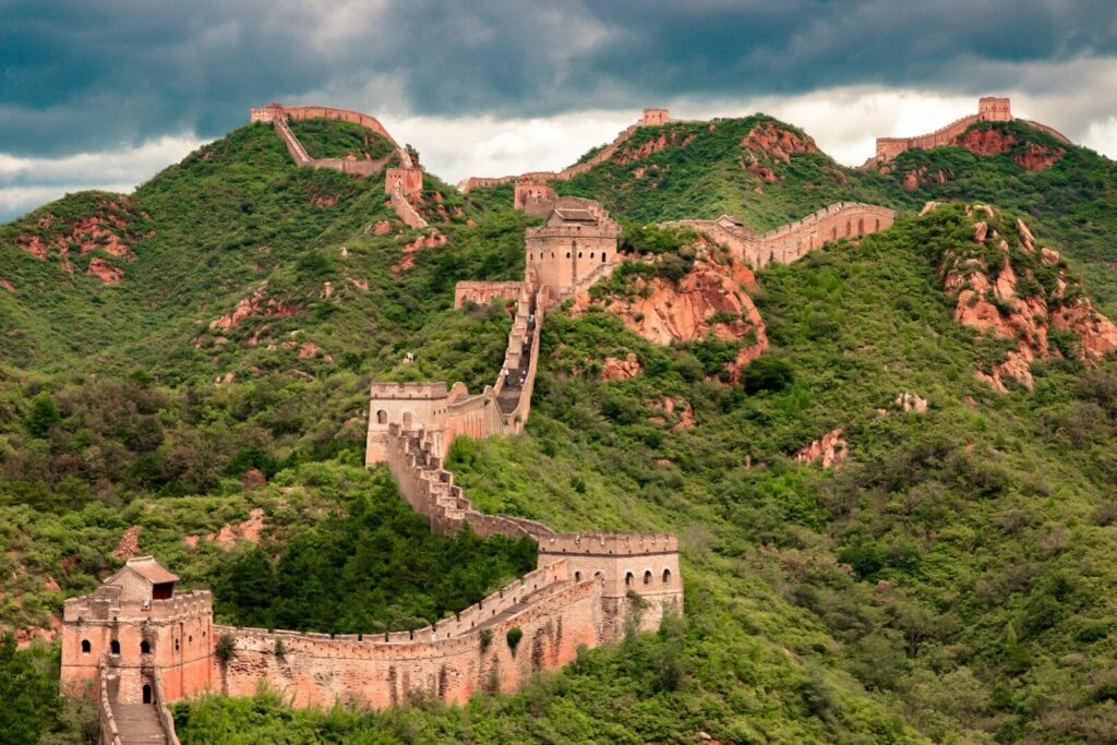 The Great Wall of China winding over green mountain ridges under a cloudy sky